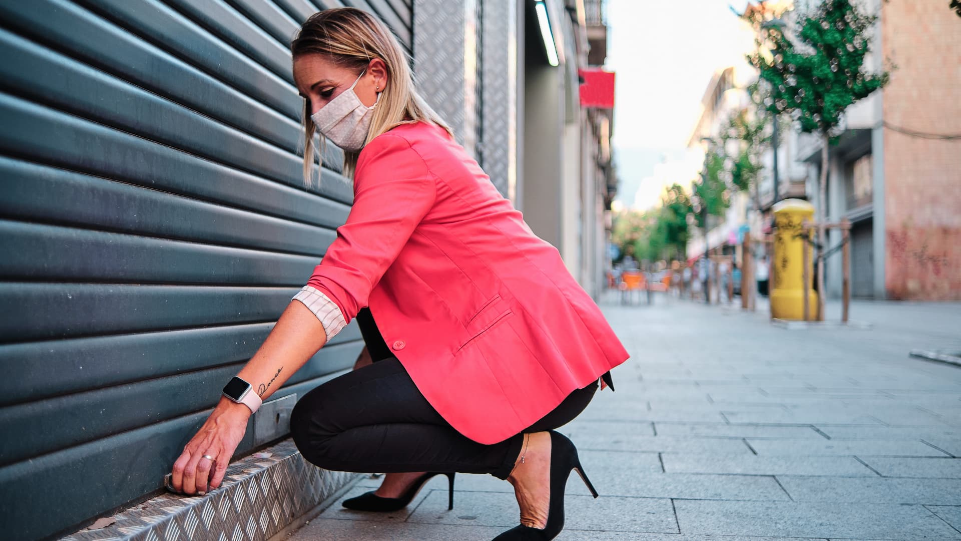 A woman kneeling to lock the gate of her business.
