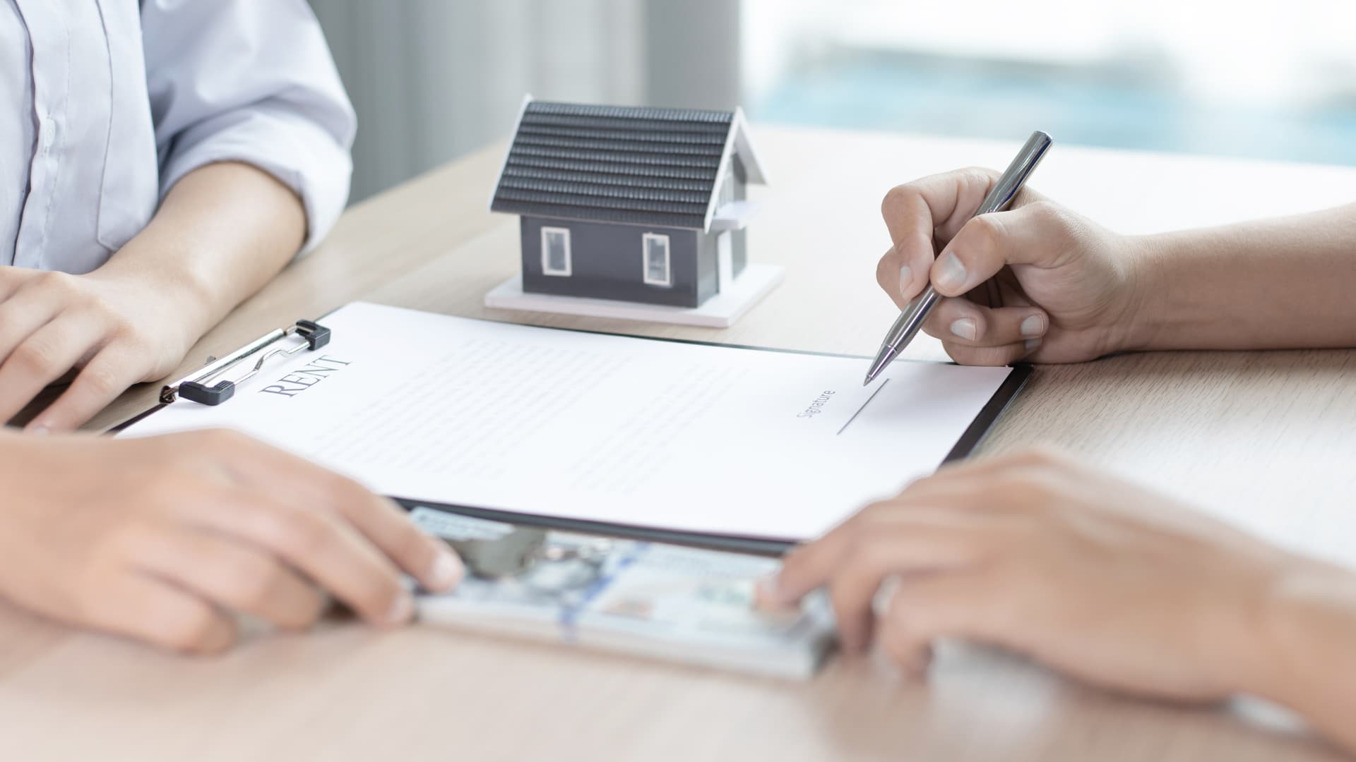 IMage of a person signing housing documents with cash in hand.