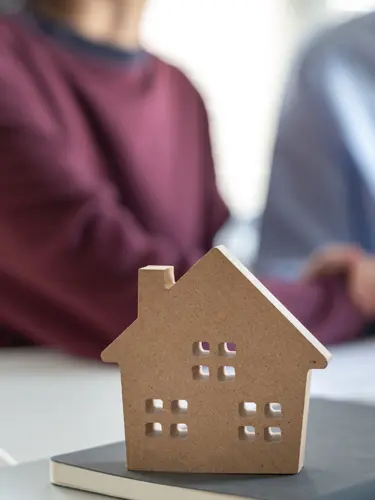 An image of a couple sitting behind a house model showing a real estate contract on the desk like those created by ASR law firm for real estate clients. 
