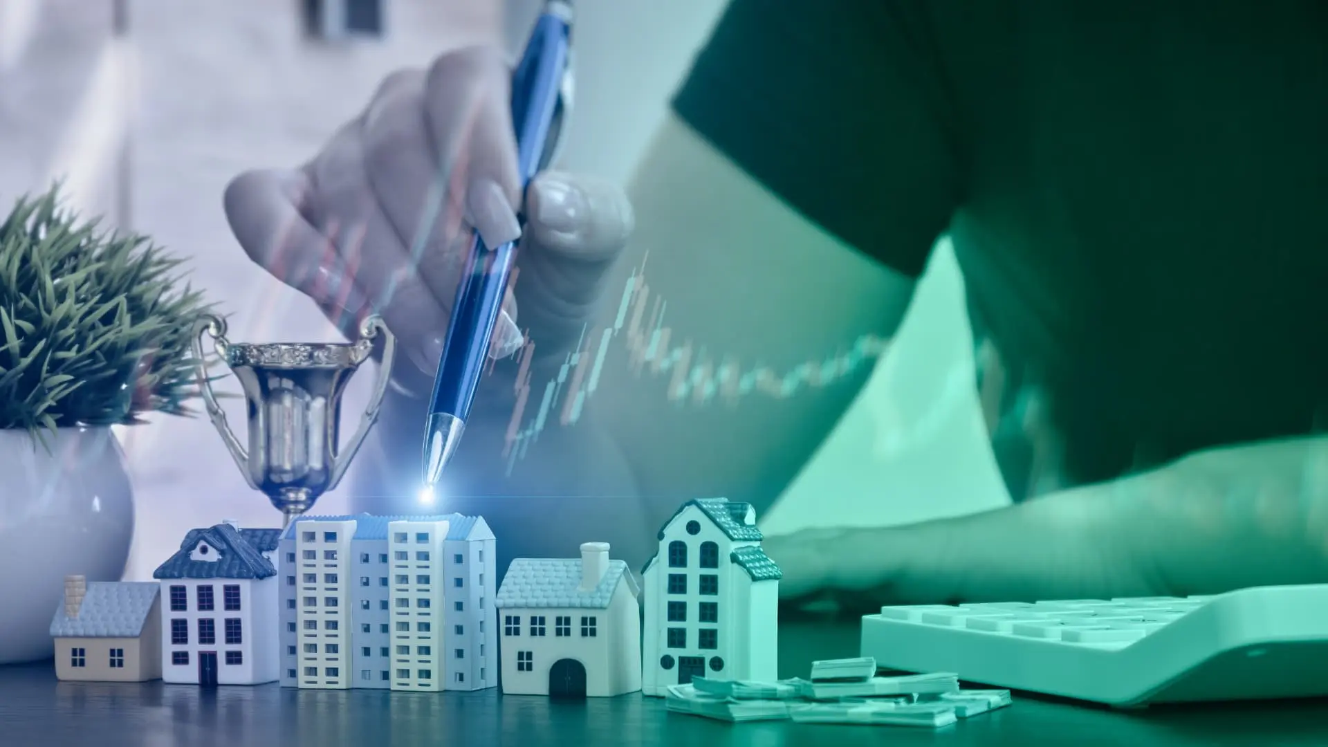 An image of house models and finances with a calculator and persons hand holding a pen. 